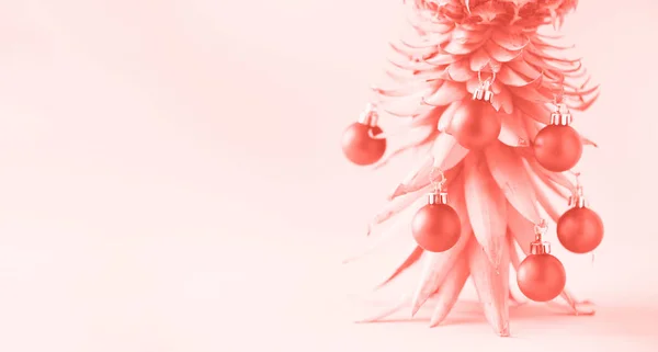 Árbol creativo de Navidad hecho de piña y adorno rojo sobre un fondo de color coral de moda, espacio para copiar. Tarjeta de felicitación, decoración para la fiesta de año nuevo. Concepto de vacaciones. Banner — Foto de Stock