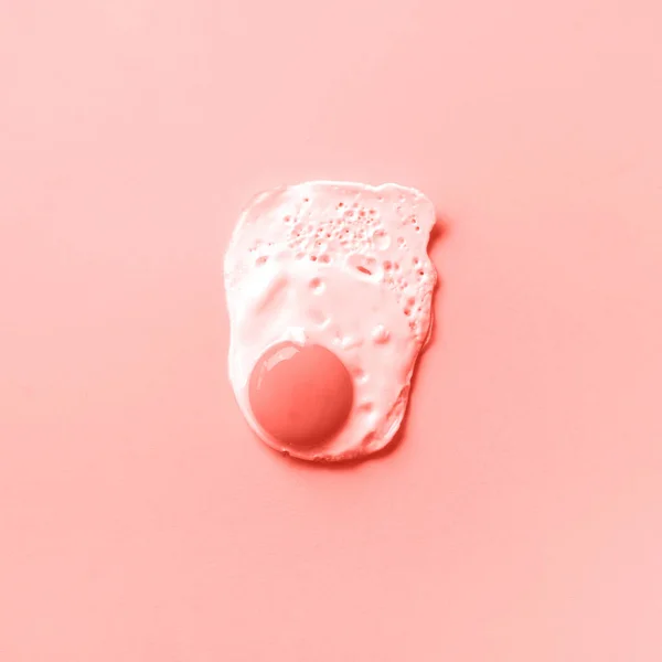 One fried egg on trendy coral color background. Creative food concept in minimal style. Top view