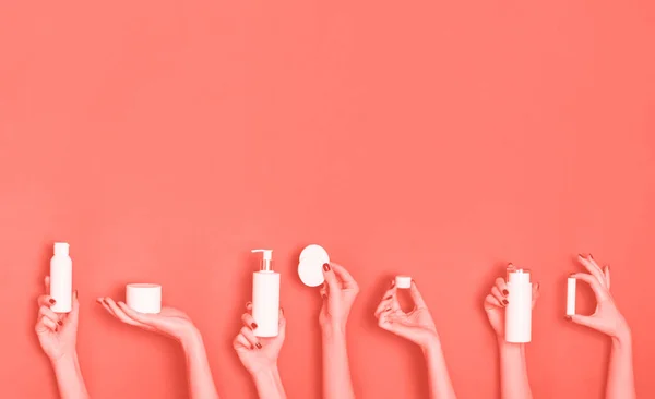 Руки женщины держат белые косметические бутылки - лосьон, крем, сыворотку на модном коралловом фоне. Квадратный. Уход за кожей, чистая красота, концепция лечения тела. Баннер с копировальным пространством — стоковое фото