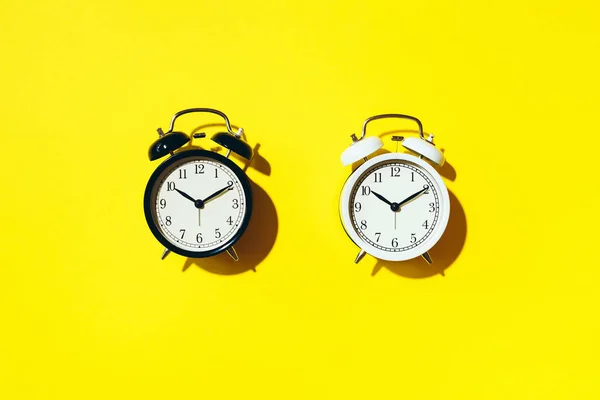 Black alarm clock and white one with hard shadow on yellow background. Top view — 스톡 사진