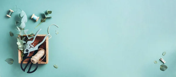 Eucalyptus branches and leaves, garden pruner, scissors, wooden boxes over green background with copy space. Florist concept, top view — 스톡 사진