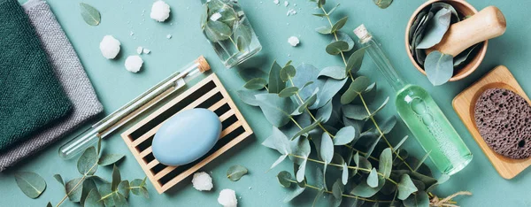 Soap, eucalyptus, towels, massage brush, salt, aroma oil and other spa objects on green background. Top view. Skin care, body treatment concept. Banner. — 스톡 사진