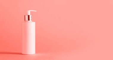 Moda cooral renk arka planında fotokopi alanı olan beyaz nemlendirici losyon şişesi. Minimalizm tarzı. Cilt bakımı, vücut bakımı, güzellik konsepti