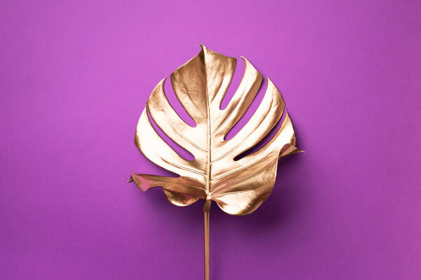 Exotic summer trend in minimal style. Golden tropical palm monstera leaf on violet color background. Shiny and sparkle design, fashion concept.