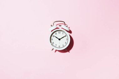 Pembe arka planda sert gölgesi olan beyaz çalar saat. Üst Manzara. Uyarı konsepti. Sabah rutini.