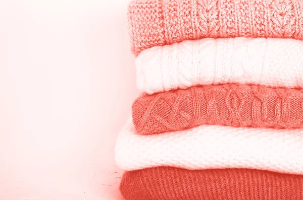 Pile of knitted wool sweaters in trendy coral color background with copy space. Knitwear, clothes — Stock Photo, Image