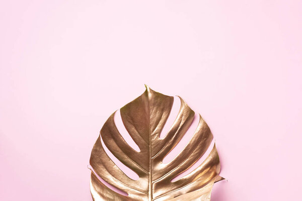Exotic summer trend in minimal style. Golden tropical palm monstera leaf on pastel pink color background. Shiny and sparkle design, fashion concept.