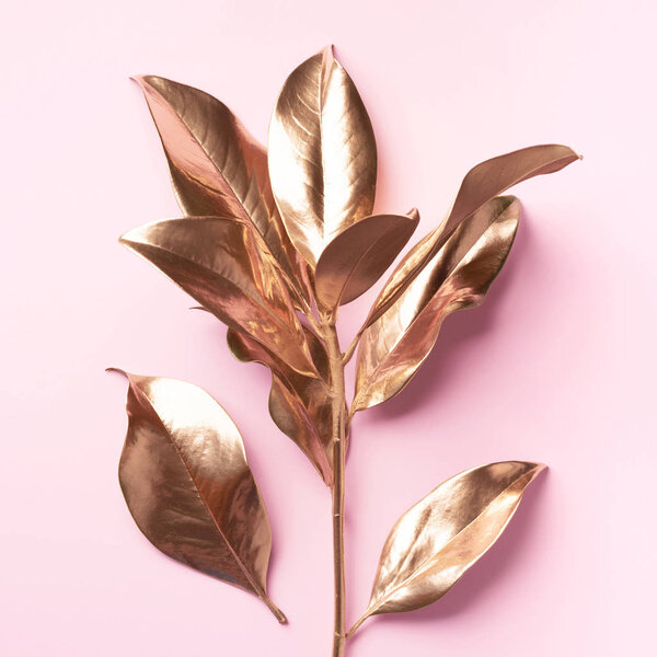 Floral minimal style concept. Exotic summer trend. Golden tropical leaves and branch on pastel pink color background. Shiny and sparkle design, fashion concept.