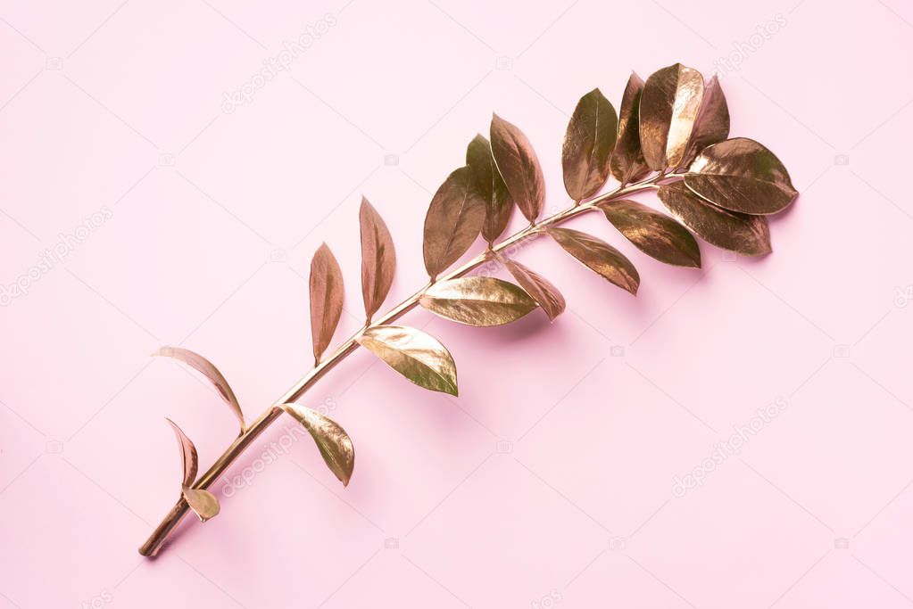 Floral minimal style concept. Exotic summer trend. Golden tropical leaves and branch on pastel pink color background. Shiny and sparkle design, fashion concept.