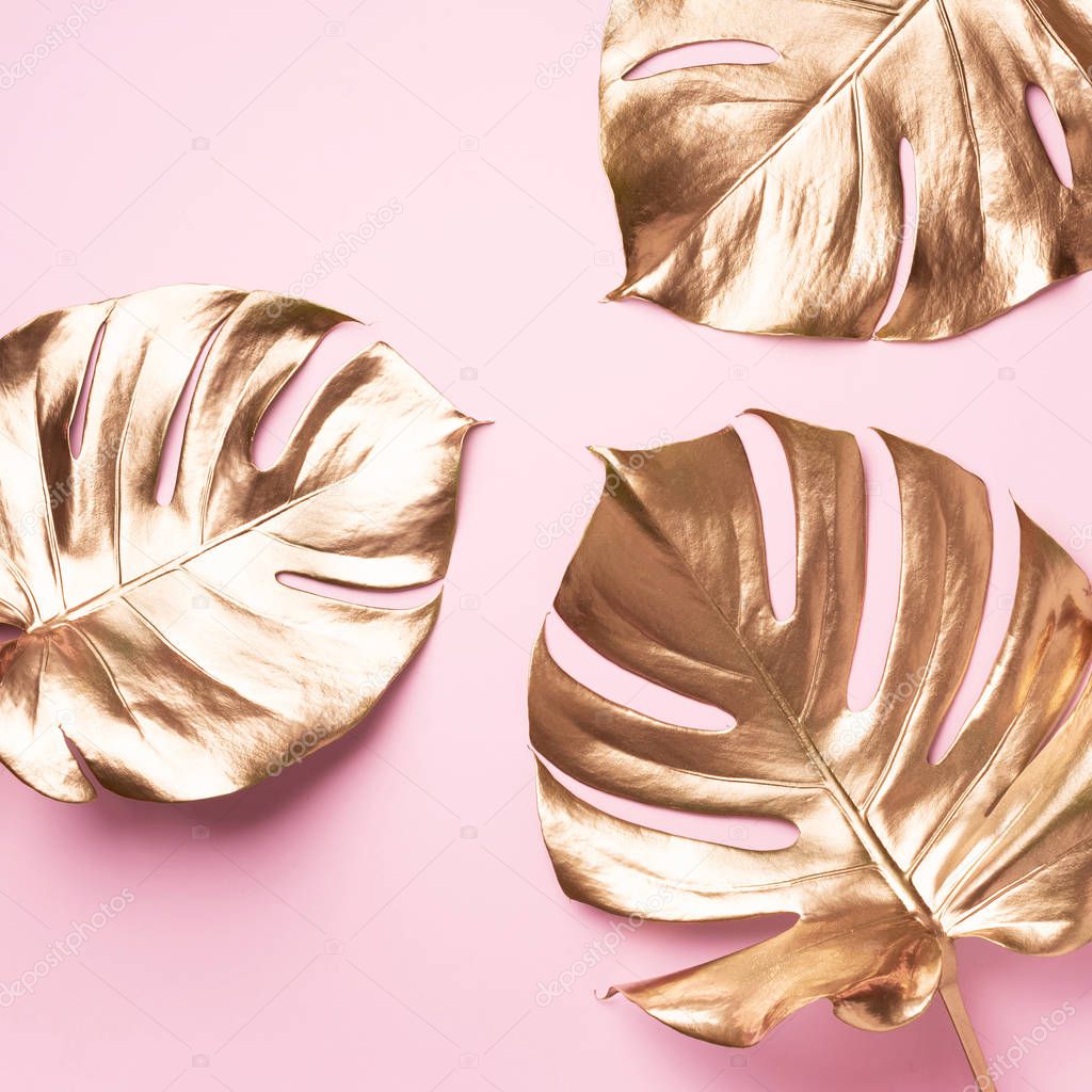 Exotic summer trend in minimal style. Golden tropical palm monstera leaf on pastel pink color background. Shiny and sparkle design, fashion concept.