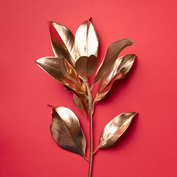 Floral minimal style concept. Exotic summer trend. Golden tropical leaves and branch on red color background. Shiny and sparkle design, fashion concept.