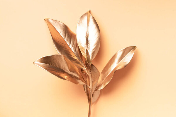 Floral minimal style concept. Exotic summer trend. Golden tropical leaves and branch on pastel nude color background. Shiny and sparkle design, fashion concept.