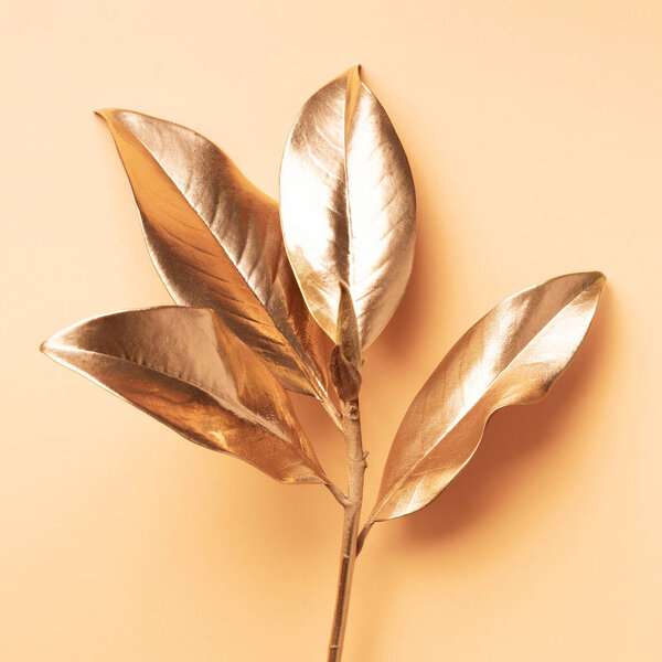 Floral minimal style concept. Exotic summer trend. Golden tropical leaves and branch on pastel nude color background. Shiny and sparkle design, fashion concept.