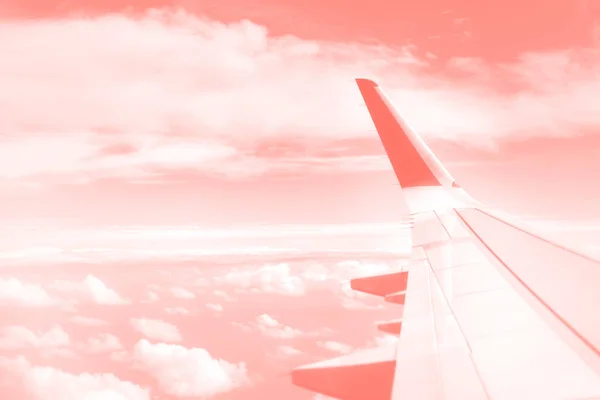 Koncepcja podróży. Skrzydło samolotu lecącego nad chmurami na modnym koralowym niebie. Przestrzeń kopiowania — Zdjęcie stockowe