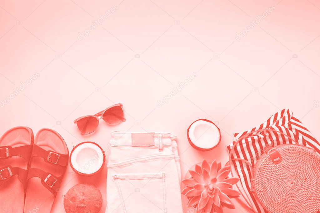 Woman summer travel clothes travel on trendy coral color background. Jeans, sneakers, bamboo bag, sunglasses, coconut and succulent. Fashion, capsule wardrobe concept.