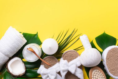 Cilt bakımı, güzellik ve kaplıca konsepti ve sarı arka planda banyo kozmetik aksesuarları. Düz yatıyordu. Beyaz havlu, bambu terlikler, krem, ahşap fırça, hindistan cevizi yağı, canavar yaprakları.