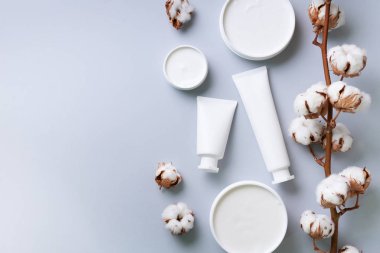 Yumuşak pamuklu çiçekler, yüz kremi, arka planda gri arkaplanda fotokopi alanı olan vücut yağı. Kozmetik, güzellik, spa konsepti. Üst Manzara. Düz yatıyordu