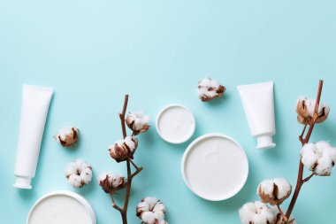Yumuşak pamuklu çiçekler, yüz kremi, mavi arka planda fotokopi alanı olan vücut yağı. Kozmetik, güzellik, spa konsepti. Üst Manzara. Düz yatıyordu