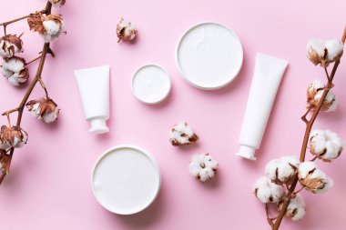 Yumuşak pamuklu çiçekler, yüz kremi, pembe arka planda fotokopi alanı olan vücut yağı. Kozmetik, güzellik, spa konsepti. Üst Manzara. Düz yatıyordu