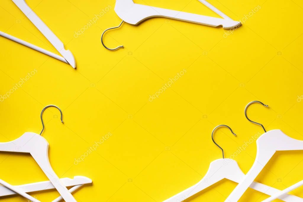 Top view of white clothes hangers on yellow background with copy space. Flat lay. Minimalism style. Creative layout. Fashion, store sale, shopping concept. Banner for feminine blog