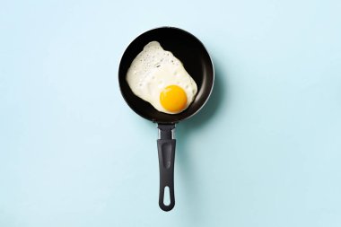 Mavi arka planda tavada pişmiş yumurta ile yaratıcı gıda konsepti. Üst Manzara. Asgari tarzda yaratıcı bir model. Düz yatıyordu