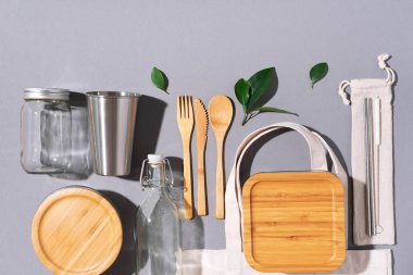 Sürdürülebilir yaşam tarzı. Sıfır atık, plastik ücretsiz alışveriş konsepti. Pamuk torbaları, cam kavanoz, şişe, metal bardak, içmek için pipet, bambu çatal bıçak takımı ve gri arka plandaki kutular..