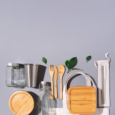 Sürdürülebilir yaşam tarzı. Sıfır atık, plastik ücretsiz alışveriş konsepti. Pamuk torbaları, cam kavanoz, şişe, metal bardak, içmek için pipet, bambu çatal bıçak takımı ve gri arka plandaki kutular..