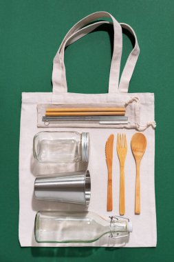 Sürdürülebilir yaşam tarzı. Sıfır atık, plastik ücretsiz alışveriş konsepti. Pamuk torbaları, cam kavanoz, şişe, metal bardak, içmek için pipet, bambu çatal bıçak takımı ve yeşil arka plandaki kutular..