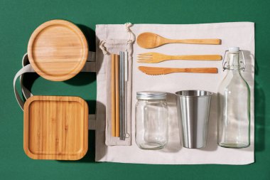 Sürdürülebilir yaşam tarzı. Sıfır atık, plastik ücretsiz alışveriş konsepti. Pamuk torbaları, cam kavanoz, şişe, metal bardak, içmek için pipet, bambu çatal bıçak takımı ve yeşil arka plandaki kutular..