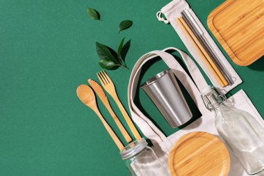 Sürdürülebilir yaşam tarzı. Sıfır atık, plastik ücretsiz alışveriş konsepti. Pamuk torbaları, cam kavanoz, şişe, metal bardak, içmek için pipet, bambu çatal bıçak takımı ve yeşil arka plandaki kutular..