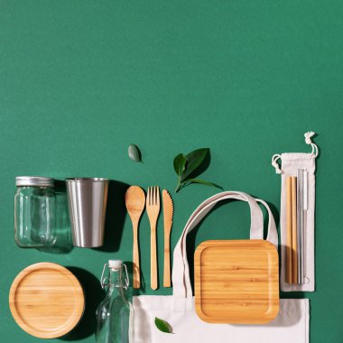 Sürdürülebilir yaşam tarzı. Sıfır atık, plastik ücretsiz alışveriş konsepti. Pamuk torbaları, cam kavanoz, şişe, metal bardak, içmek için pipet, bambu çatal bıçak takımı ve yeşil arka plandaki kutular..