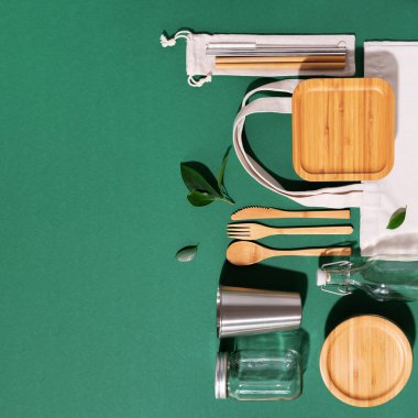 Sürdürülebilir yaşam tarzı. Sıfır atık, plastik ücretsiz alışveriş konsepti. Pamuk torbaları, cam kavanoz, şişe, metal bardak, içmek için pipet, bambu çatal bıçak takımı ve yeşil arka plandaki kutular.