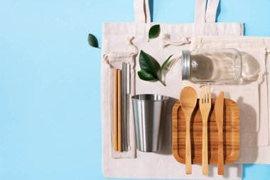 Sürdürülebilir yaşam tarzı. Sıfır atık, plastik ücretsiz alışveriş konsepti. Pamuk torbaları, cam kavanoz, şişe, metal bardak, içmek için pipet, bambu çatal bıçak takımı ve mavi arka plandaki kutular.