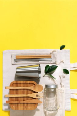 Sürdürülebilir yaşam tarzı. Sıfır atık, plastik ücretsiz alışveriş konsepti. Pamuk torbaları, cam kavanoz, şişe, metal bardak, içmek için pipet, bambu çatal bıçak takımı ve sarı arka plandaki kutular..
