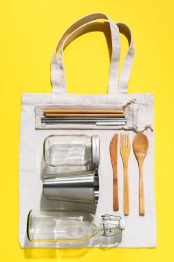 Sürdürülebilir yaşam tarzı. Sıfır atık, plastik ücretsiz alışveriş konsepti. Pamuk torbaları, cam kavanoz, şişe, metal bardak, içmek için pipet, bambu çatal bıçak takımı ve sarı arka plandaki kutular..