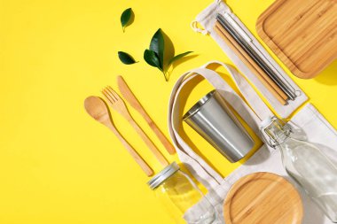 Sürdürülebilir yaşam tarzı. Sıfır atık, plastik ücretsiz alışveriş konsepti. Pamuk torbaları, cam kavanoz, şişe, metal bardak, içmek için pipet, bambu çatal bıçak takımı ve sarı arka plandaki kutular..