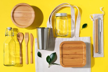 Sürdürülebilir yaşam tarzı. Sıfır atık, plastik ücretsiz alışveriş konsepti. Pamuk torbaları, cam kavanoz, şişe, metal bardak, içmek için pipet, bambu çatal bıçak takımı ve sarı arka plandaki kutular..