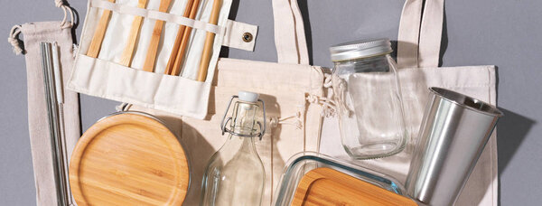 Cotton bags, glass jar, bottle, metal cup, straws for drinking, bamboo cutlery and boxes on gray background. Sustainable lifestyle. Zero waste, plastic free shopping concept.
