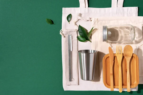 Sustainable lifestyle. Zero waste, plastic free shopping concept. Cotton bags, glass jar, bottle, metal cup, straws for drinking, bamboo cutlery and boxes on green background. — Stock Photo, Image