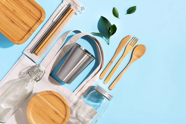 Sürdürülebilir yaşam tarzı. Sıfır atık, plastik ücretsiz alışveriş konsepti. Pamuk torbaları, cam kavanoz, şişe, metal bardak, içmek için pipet, bambu çatal bıçak takımı ve mavi arka plandaki kutular.