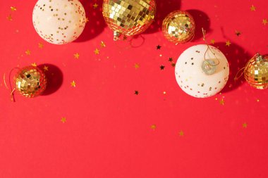 Noel kompozisyonu. Düz yerde, üst tarafta. Disko topu takısı, yıldız pırıltısı. Asgari yeni yıl partisi konsepti. Kırmızı arkaplanda fotokopi alanı olan beyaz ve altın Noel süslemeleri.