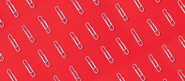 Pattern of white paper clips on red background. Back to school. Office, business, paperwork, education concept. Banner