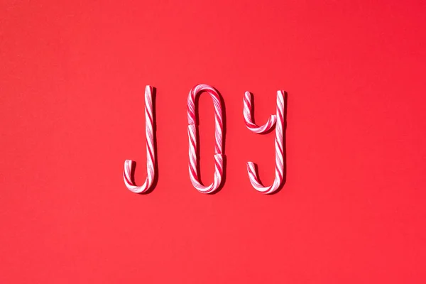 Joy word written with Christmas candy canes on red background. Top view. Flat lay. New year and Christmas concept — Stock Photo, Image