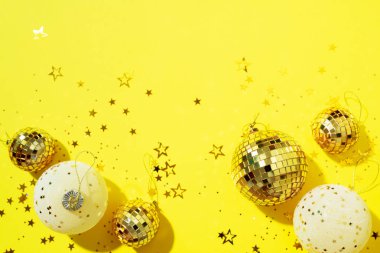 Noel kompozisyonu. Düz yerde, üst tarafta. Disko topu takısı, yıldız pırıltısı. Asgari yeni yıl partisi konsepti. Sarı zemin üzerinde noel beyazı ve altın süslemeler kopya alanı ile.