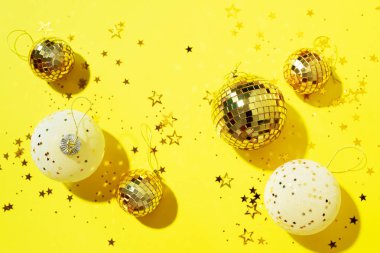 Noel beyazı ve altın süslemeler, ayna disko topları, sarı arka planda yıldız parıltısı. Düz yerde, üst tarafta. Asgari yeni yıl partisi konsepti. Kopya alanı olan Noel tebrik kartı