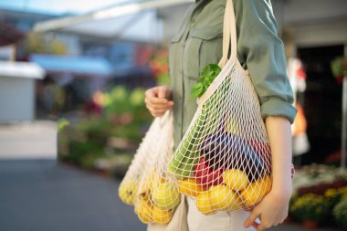 Girl holding mesh shopping bag and cotton shopper with vegetables without plastic bags at farmers market. Zero waste, plastic free concept. Sustainable lifestyle. Banner. clipart