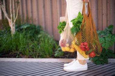 Kopya alanı ile sıfır atık kavramı. Elinde pamuk alışverişi yapan bir kadın ve sebze ve ürünlerle tekrar kullanılabilir ağ alışveriş torbaları. Çevre dostu ağ tüccarı. Sıfır atık, plastiksiz konsept.