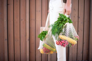 Naylon poşetsiz, ahşap arka planda sebzeli pamuk alışverişi yapan kız. Sıfır atık, plastiksiz konsept. Sürdürülebilir yaşam tarzı. Pankart.