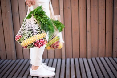Naylon poşetsiz, ahşap arka planda sebzeli pamuk alışverişi yapan kız. Sıfır atık, plastiksiz konsept. Sürdürülebilir yaşam tarzı. Pankart.