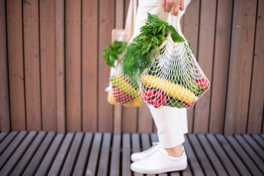 Kopya alanı ile sıfır atık kavramı. Elinde pamuk alışverişi yapan bir kadın ve sebze ve ürünlerle tekrar kullanılabilir ağ alışveriş torbaları. Çevre dostu ağ tüccarı. Sıfır atık, plastiksiz konsept.